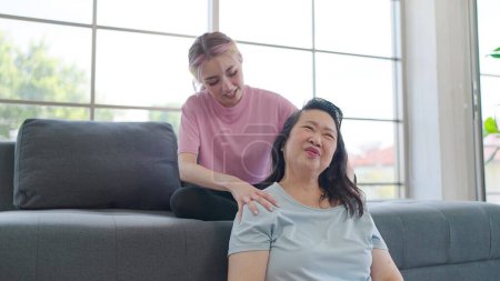 Foto de Hija asiática dando masaje en el hombro a la madre anciana mientras relexing en la sala de estar en casa. Hija joven dando un masaje relajante madre anciana. Estilo de vida familiar - Imagen libre de derechos