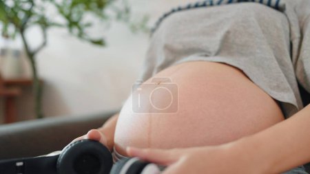 Téléchargez les photos : Femme enceinte relaxante tenant casque audio thérapie bébé à naître. Les femmes enceintes tenant des écouteurs jouent de la musique pour bébé dans le ventre. Concept de grossesse - en image libre de droit