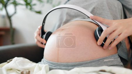 Photo for Relaxing pregnant woman holding headphones putting on belly audio therapy unborn baby. Women pregnant putting headphone play music for baby in belly. Pregnancy concept - Royalty Free Image