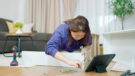 Téléchargez les photos : Les jeunes femmes asiatiques à l'aide serre vis pour assembler de nouveaux meubles par elle-même à la maison. Assemblage de meubles concept - en image libre de droit