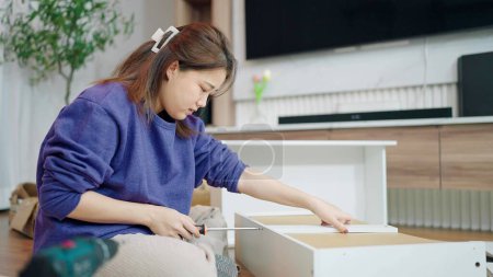 Foto de Jóvenes mujeres asiáticas que utilizan aprieta tornillo para montar nuevos muebles por sí misma en casa. Montaje del concepto de mobiliario - Imagen libre de derechos