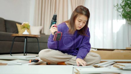 Photo for Young asian women holding a drill for assembling new furniture by herself at home. Woman sitting on floor in living room holding a drill for assembling furniture. Assembling furniture concept - Royalty Free Image