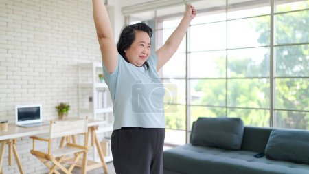 Téléchargez les photos : Femme asiatique senior faisant des exercices de réchauffement à la maison. Femme âgée active faisant de l'exercice des bras à la maison. Personnes âgées Sportif concept de style de vie - en image libre de droit