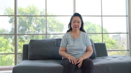 Téléchargez les photos : Femme âgée asiatique solitaire assise sur un canapé à la maison. Malade femme âgée ayant une dépression ou des étourdissements alors qu'elle était assise seule dans le salon à la maison. Concept de problème de santé - en image libre de droit