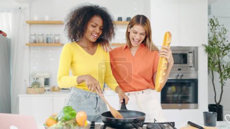 Photo for Happy young woman friends enjoy singing and dancing while cooking at kitchen room. Lesbian couple having fun singing dancing together while cooking together at home - Royalty Free Image