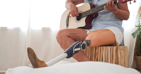 Téléchargez les photos : Gros plan jambe prothétique des femmes amputées aiment jouer guitare acoustique détente à la maison. des femmes en prothèse de jambe jouant de la guitare. Équipement de prothèse de jambe, concept Amputé - en image libre de droit