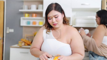 Téléchargez les photos : Chubby femmes asiatiques se sentent tristes tout en cuisinant, préparer le dîner dans la salle de cuisine à la maison. Positivité du corps. Concept d'acceptation corporelle - en image libre de droit