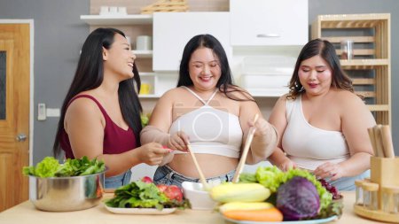 Téléchargez les photos : Groupe de femmes asiatiques joyeux plus la taille aiment cuisiner, préparer le dîner dans la salle de cuisine à la maison. Positivité du corps. Concept d'acceptation corporelle - en image libre de droit