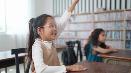 Photo for Active excellent Asian student schoolgirl in glasses raising hands up answer the questions in classroom at school. Portrait of children studying in classroom at the school. Children learning concept - Royalty Free Image