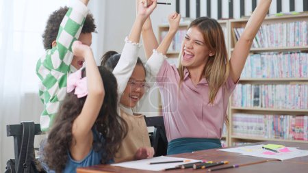 Photo for Happy schoolkids and women teacher raising hands together after finish a lesson in classroom. Back to school concept, Education and learning concept - Royalty Free Image