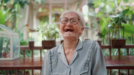 Foto de Retrato feliz Asiática mujer mayor riendo, sonriendo y mirando a la cámara mientras se sienta en casa. Adultos mayores estilo de vida, personas mayores y concepto de relajación - Imagen libre de derechos