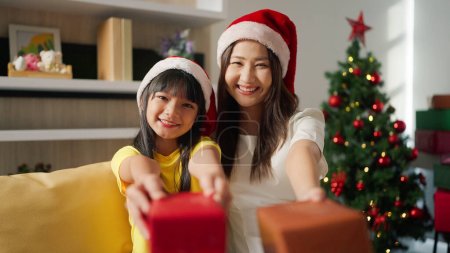Photo for Christmas family celebration. Happy asian woman and little girl with gift in santa claus hats at home. Mother and daughter holding gifts and smiling to camera Family enjoy winter holidays - Royalty Free Image