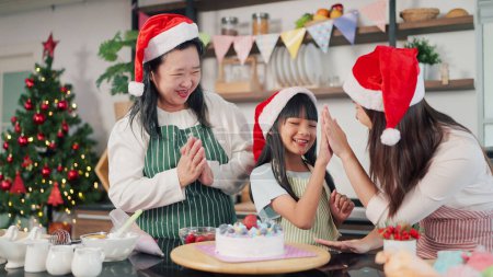 Foto de Feliz abuela, madre e hija pequeña decoraron el pastel juntos para Nochebuena. Tres generaciones de mujeres asiáticas haciendo tarta para el día de Navidad. Pastel de Navidad decorado. Vacaciones festivas - Imagen libre de derechos