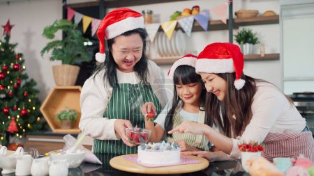 Photo for Happy Grandmother, mother and little daughter decorated cake together for Christmas Eve. Three generations Asian women making cake for Christmas day. Christmas cake decorated. Festive holiday - Royalty Free Image