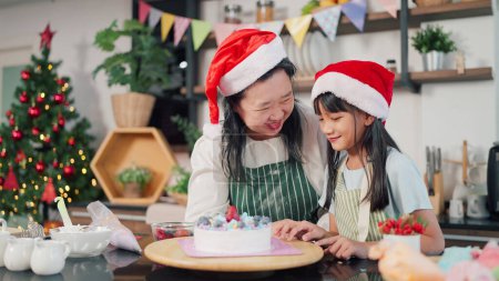 Photo for Happy Grandmother and granddaughter playful while making cake for Christmas day in kitchen room at home. Christmas cake decorated. Festive holiday. Family and cooking concept - Royalty Free Image