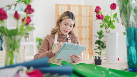 Photo for Small business concept. Young asian woman florist using tablet writing on order online at flower shop. Female florist or flower shop owner using tablet working, receiving order at flower shop - Royalty Free Image