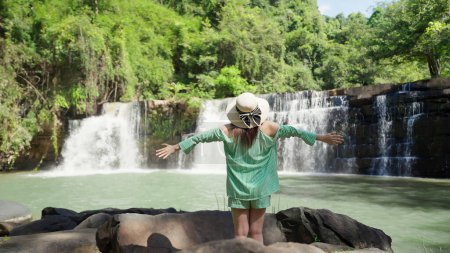 Photo for Back view of female tourist raised hands into the air looking at beautiful waterfall. Happy woman traveler enjoy beauty nature and waterfall on sunny day. Nature and travel. Beautiful nature concept - Royalty Free Image