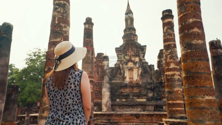 Foto de Sitios antiguos, atracciones turísticas en Sukhothai, Tailandia. Vista trasera de la mujer turística que camina en el templo de Wat Mahatat, parque histórico de Sukhothai, Sukhothai, Tailandia. UNESCO Patrimonio de la humanidad - Imagen libre de derechos