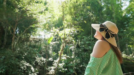 Foto de Feliz joven mujer asiática viajero disfrutar de la belleza de la naturaleza en el bosque verde. Turista femenina buscando y relajarse con aire fresco en el bosque verde. Naturaleza y viajes. Hermoso concepto de naturaleza - Imagen libre de derechos