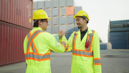 Foto de Dos ingenieros asiáticos o capataz estrechando la mano después de trabajar en el puerto de carga de contenedores para cargar contenedores. Dos trabajadores dando la mano para el éxito trabajando en el puerto de carga de contenedores. Trabajo en equipo - Imagen libre de derechos