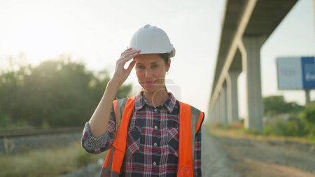 Photo for Beautiful engineer woman in safety uniform and helmet standing on railroad smiling and looking at camera. Engineer leadership concept - Royalty Free Image