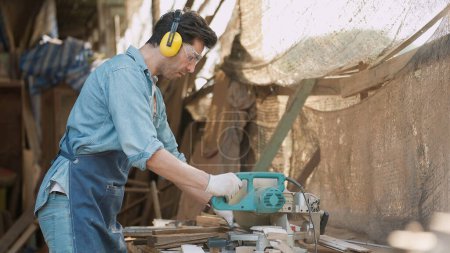 Photo for A male carpenter using a circular saw to cut wood for making new furniture at wood workshop. Carpenter using a circular saw making woodcraft furniture. Carpenter and woodcraft concept - Royalty Free Image