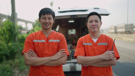 Foto de Retrato de dos paramédicos. Dos paramédicos asiáticos en uniforme de pie con los brazos cruzados detrás de la ambulancia sonriendo a la cámara. EMS Paramédico - Imagen libre de derechos