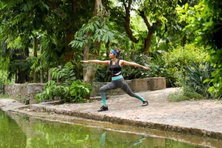 Woman exercising standing in virabhadrasana yoga pose in park
