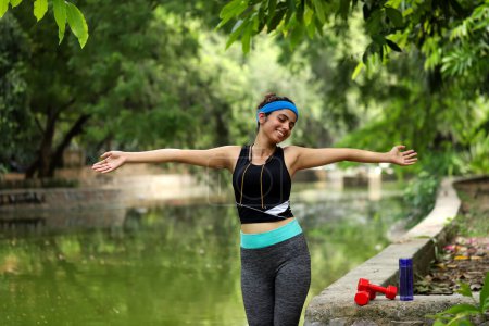 Sexy lady in gym outfit breathing morning fresh air raising arms after workout in garden
