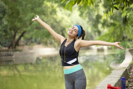 Athletic woman inhaling fresh air after workout in garden over blur nature background