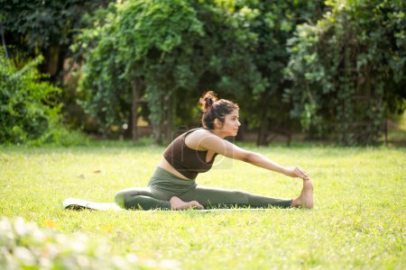 Superb girl doing head to knee pose (Janu Sirsasana) yoga pose in park