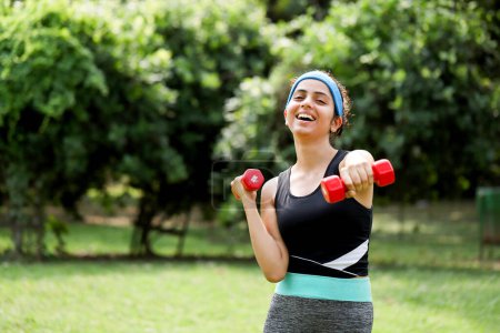 Lady working out with red dumbbells in hand in park