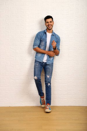Sexy man with beard wearing a white t-shirt with a denim jacket and posing against white wall