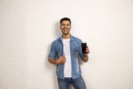 Ein eleganter Mann in Jeanshemd zeigt lächelnd sein Handy in die Kamera. Adverstimmendes Konzept