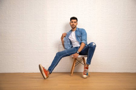 Lovely man wearing denim shirt and blue jeans is posing in front of camera against white background