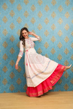 Eine junge indische Frau im traditionellen Anzug lächelt, während sie auf einem Bein posiert