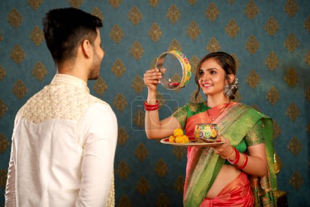 Photo shows a young Asian couple celebrating the Karwa Chauth festival while dressed traditionally in Indian garb