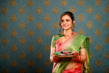 Eine hübsche junge Hausfrau feiert Diwali, während sie einen Puja-Teller in der Hand hält, während sie einen traditionellen indischen Sari anzieht