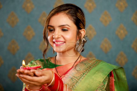 Foto de una joven y bonita modelo vestida con atuendo tradicional indio y sosteniendo una diya durante la celebración de Diwali