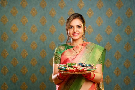 Stock photo of a nicewoman wearing a traditional Indian saree and holding a tray of diyas during the festival of Diwali