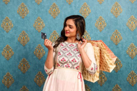 Eine hinreißend gekleidete indische Frau mit EC-Karte und Einkaufstaschen in der Hand