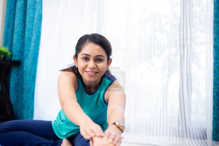 entusiasta del yoga realizando ejercicio de estiramiento isquiotibial sentado en la esterilla en casa