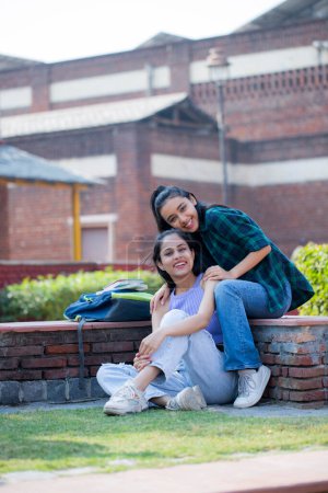 Two sweet girls are smiling while sitting in the univeristy park