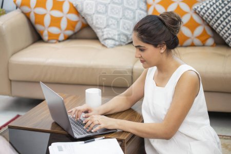 Mujer más guapa trabajando en el ordenador portátil mientras está sentado en el suelo en la sala de estar en casa