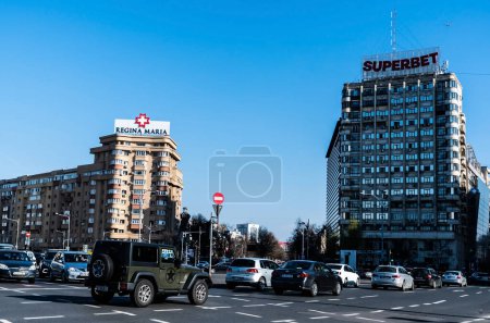 Foto de BUCHAREST, RUMANIA - 19 DE MARZO DE 2023: Plaza de la Victoria con los logos de Regina Maria y Superbet en los edificios residenciales. - Imagen libre de derechos