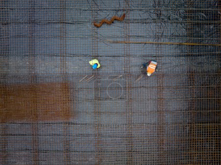 Foto de Construcción como arte: una vista aérea perpendicular de una malla de acero reforzado y dos trabajadores que trabajan en la obra. Geometría en construcción. Usando el dron para comprobar el progreso. - Imagen libre de derechos