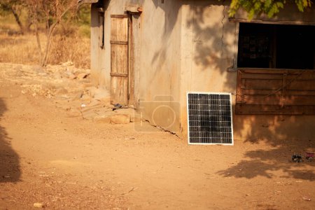 Foto de Un pequeño panel fotovoltaico apoyado en la esquina de una cabaña de tierra, cargando un teléfono móvil. África, Madagascar - Imagen libre de derechos