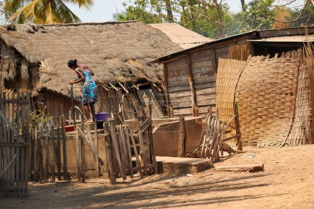 Foto de Abastecimiento de agua en África. Una mujer malgache saca agua con una bomba de pie primitiva de un pozo, cabaña de madera, pueblo. Vida auténtica en Madagascar. - Imagen libre de derechos