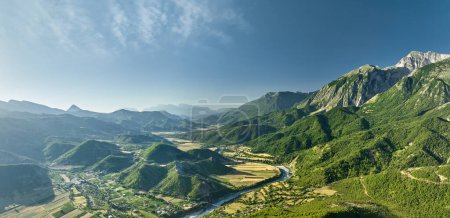 Téléchargez les photos : Aerial panoramic view of the Vjose River valley in Albania. The crystal clear, turquoise river winds its way through fields against a backdrop of majestic mountains. Blue skies, summer. - en image libre de droit