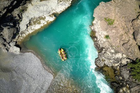 Téléchargez les photos : Aventures de rafting en eaux vives : Un radeau jaune flottant parmi les rochers sur les eaux cristallines et bleu-vert de la rivière Vjose, en Albanie. Vue par drone perpendiculaire des chevrons flottant sur la rivière. - en image libre de droit